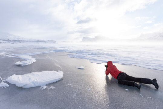 Man photographing the snowy landscape lying down on a frozen lake, Stora Sjofallet, Norrbotten County, Lapland, Sweden, Scandinavia, Europe