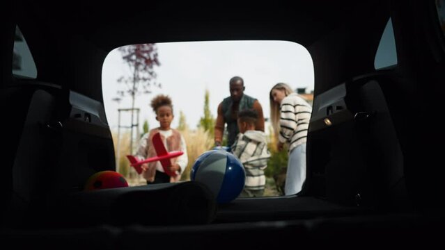Young multiracial family packing their stuff in electric car, preparing for family trip.