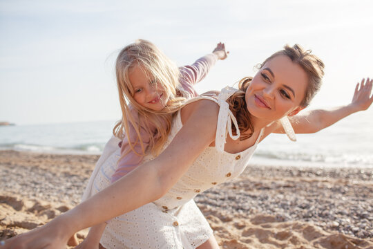 Mither holds the doughter hand and walks in the baech together against the background the sea or coean