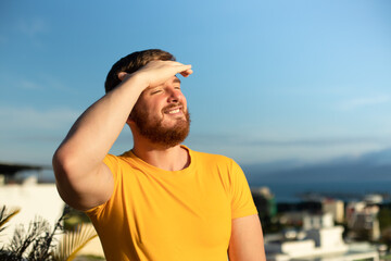 Portrait of happy cheerful positive guy, young handsome bearded man with beard is enjoying sunny day, summer vacation, sunbathing, tanning at sun and smiling, breathing deep, inhale fresh air