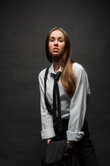 brunette woman with long hair standing in suit with suspenders while holding blazer on black.