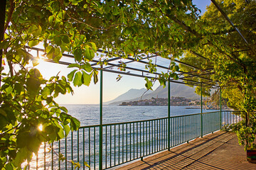 terrace on the beach with a pergola twined with grapes. View of the sea, the mountains and the small town on a clear sunny day