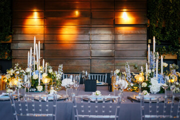 Table setting decorated with a gray tablecloth, silver plates, blue napkins and compositions of white, blue flowers and candles. Concept of wedding decorations 
