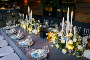 Table setting decorated with a gray tablecloth, silver plates, blue napkins and compositions of white, blue flowers and candles. Concept of wedding decorations 