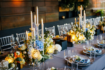 Close-up of a festive table setting. Silver plate decorated with a blue napkin and white natural roses on a gray tablecloth. Wedding decoration concept 
