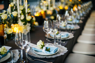 Table setting decorated with a gray tablecloth, silver plates, blue napkins and compositions of white, blue flowers and candles. Concept of wedding decorations 