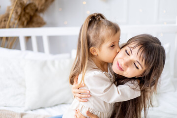 Obraz na płótnie Canvas a little baby girl with her mom hugging and kissing at home on the bed. Lifestyle. Happy family and motherhood. International Women's Day or Mother's Day. High-quality photography