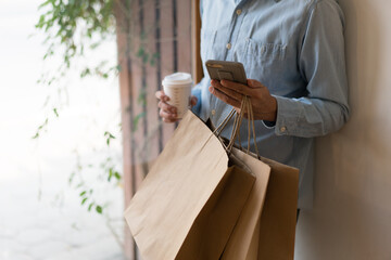 Close up of man`s hand holding smart phone research shopping  mall and shopping bags while walking on the street.