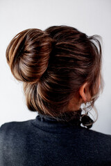 Naklejka premium The back view of girl has an evening professional hairstyle made of her brunette hair. The woman is wearing hanging earrings