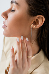 close up view of pretty young woman with closed eyes and golden jewelry posing isolated on grey.