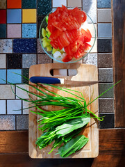 Chopped vegetables and a cutting board with a knife. on top of a plate with tomatoes and cucumbers, green onions and sorrel on the board. - 569633486