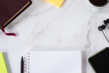 Blank notebook, holy bible book, earphones, smartphone, paper notes, and cup of coffee on white marble background. Top table view. Copy space for text. Christian study, biblical education concept.