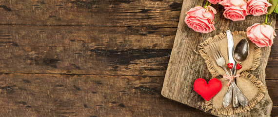Rustic table setting for romantic dinner. Bouquet of fresh roses, cutlery and heart