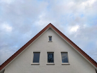 Konzept Wohnungsmarkt oder Hausbau: Frontalansicht auf den Giebel eines neuen oder frisch sanierten Hauses mit heller Fassade und Fenstern mit Himmel und viel Copy Space