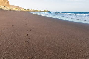 Scenic view on beach Playa Valle Gran Rey during sunset seen from Promenade de Playa de La Calera in Valle Gran Rey on La Gomera, Canary Islands, Spain, Europe. Foot prints in dark volcanic sand beach