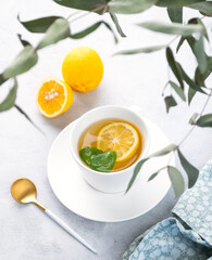 Herbal tea with lemon and mint in a white cup on a light background with eucalyptus branches. The concept of a healthy and delicious breakfast drink for immunity.