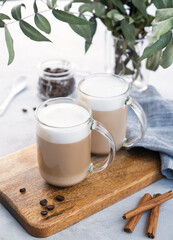 Two cappuccino or latte with milk foam in glasses on a light blue background with coffee beans, cinnamon and eucalyptus branch.