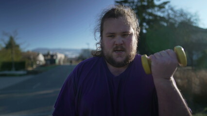 One disciplined young fat man lifting dumbbells outdoors. Motivational concept of an overweight person getting back into shape