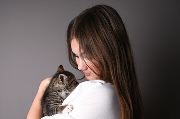Young girl holding a baby cat on gray background. Female hugging her cute kitty. Adorable domestic pet concept.
