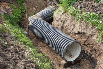 a wide black pipe lies in a ditch in the summer