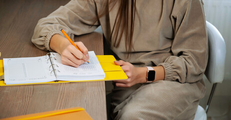 Beautiful female hands write a pen in a notebook of tasks and goals on a wooden table