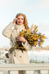 A young woman stands with a bouquet of yellow mimosa and sniffs the flowers. The concept of the Spring holiday - March 8, Easter, Women's Day.