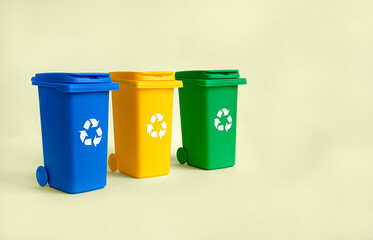 Blue, yellow and green container for separate plastic, paper and organics garbage collection, isolated on the yellow background with copy space, waste recycling concept