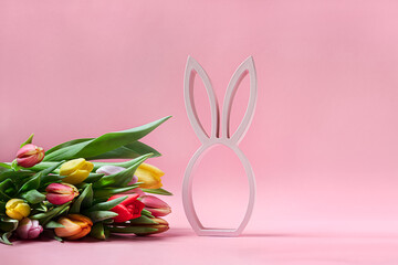 Wooden figurine of easter bunny and bouquet of spring tulips on pink background, easter minimal concept with copy space