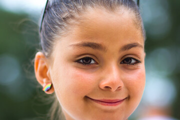 A large portrait on a green background with a side of a swarthy tanned Caucasian Armenian girl of 10 years old, who smiles and gives good. Selective focus on the eyes.