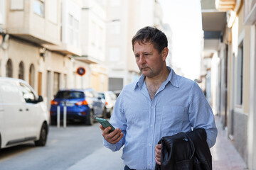 A serious businessman man talks on a mobile phone on the street, in the city