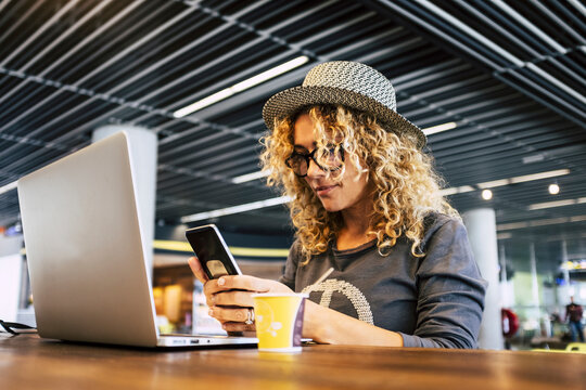 Image of traveler young trendy woman working with mobile phone and laptop in cafe bar coworking free wireless connection. Smart working lifestyle female people. Alternative businesswoman job indoor