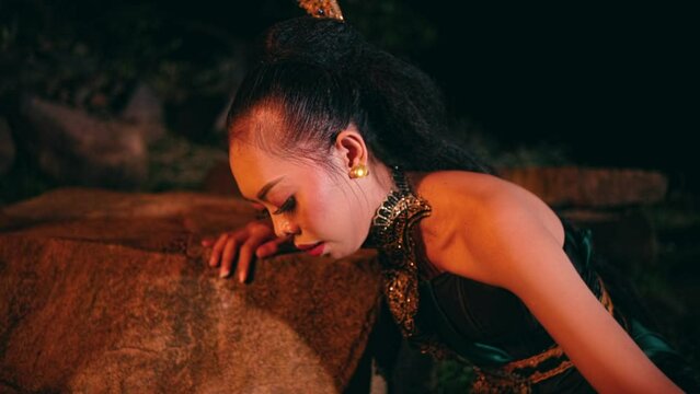 An Asian woman cries when she is about to sit on a rock helplessly and leans against a rock in the middle of a forest