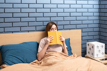 Young attractive woman sitting on the bed and reading book before going to sleep