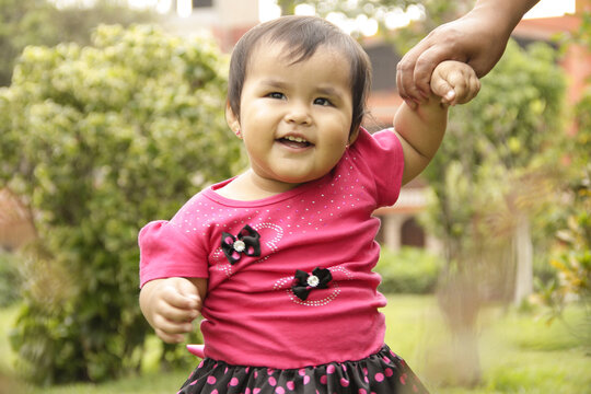 NI&Ntilde;A CON VESTIDO ROSA EN UN PARQUE JUGANDO Y SONRIENDO,TOMADA DE LA MANO DE SU MADRE, CONCEPTO DIA DEL NI&Ntilde;O Y CRECIMINETO Y DESARROLLO INFANTIL