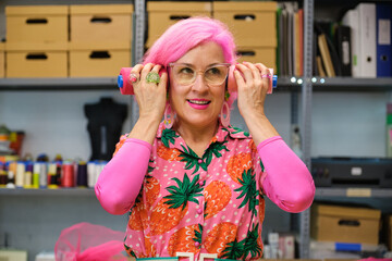 Tailor with pink hair and colorfull clothes making funny faces with sewing thread reels in a sewing...