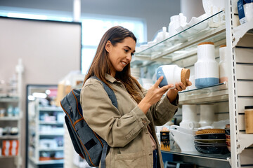 Young happy woman buying crockery at retail store.