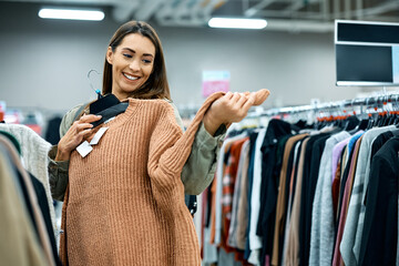 Happy woman trying on sweater while shopping at clothing store.