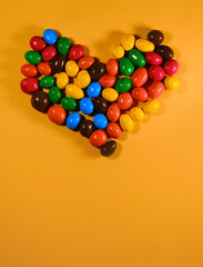 Concept of Valentine's Day. View from above. Flatlay greeting card with copy space. Colorful sweet candies are laid out in the shape of a heart. Yellow background.
