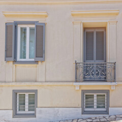 A light ocher colored house front with grey windows and a balcony. Travel to Anafiotika "Athens island" neighborhood, Greece.