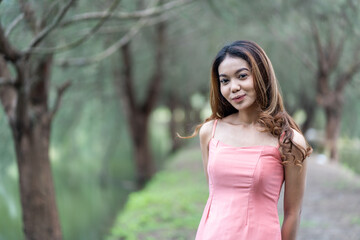 Fototapeta premium Young woman in pink dress enjoying the tranquility with bokeh park background