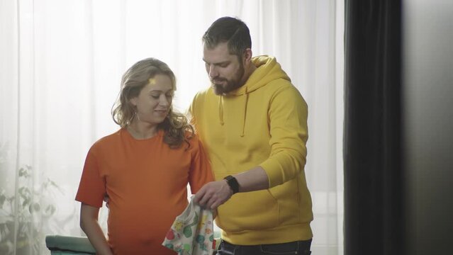 Happy pregnant family. A man and a woman are expecting a child. People smile and try on baby clothes on mom's stomach.