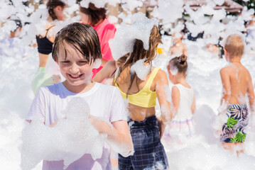happy little boy with foam on his head, in wet clothes at a foam party or holiday on a sunny hot...