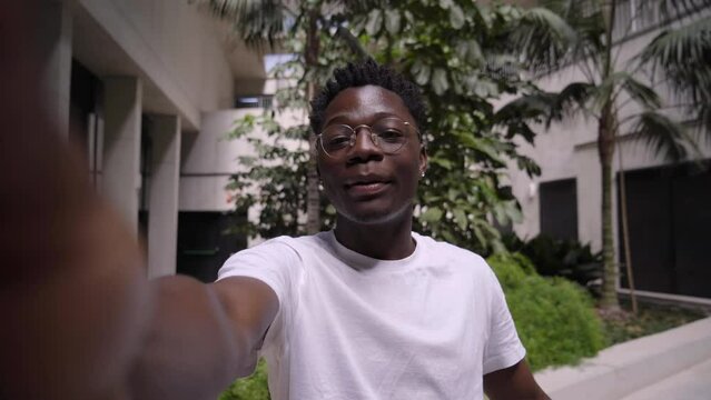 POV young African American smiling and cheerful young man talking to camera on video call. Happy people looking at mobile outside. Black man recording himself with cell phone and pointing something. 