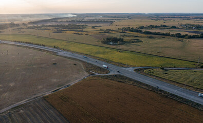 the highway curves in a turn on a U-turn. The track goes between the fields against the backdrop of the sunset sky. Cars are driving along the road. Drone photo