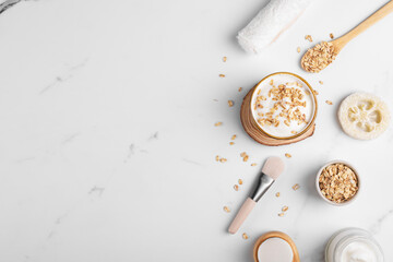 Homemade facial mask or creamy scrub with cereal, made of yogurt and oats flake, home spa cosmetics on a white marble background with natural beauty treatment ingredients and towel, flat lay, top view
