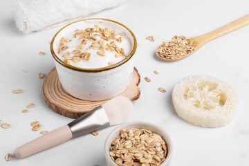 Homemade facial mask or creamy scrub with cereal made of yogurt and oats flake on a white marble background