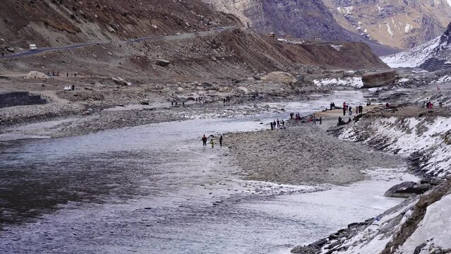 crowd of people in winter wear playing in on the river side in beautiful valley with barren himalaya mountains around in lahul, manali solang a popular tourist spot during winters