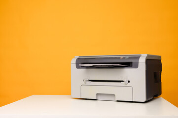 Front view of a light printer and a blank A4 paper on a white table on a yellow background,...
