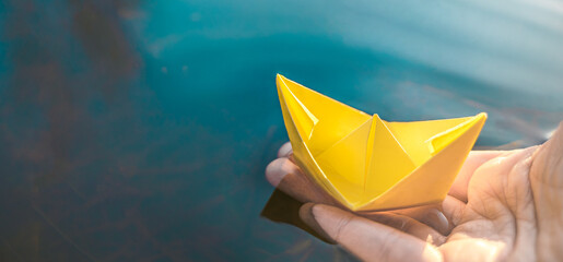 Yellow lonely floating paper boat in hand. Colorful sailing ship in big blue spring puddle, river water.Warm wet rainy weather.Hello spring,autumn.Children play,have street fun outdoors.Way to future