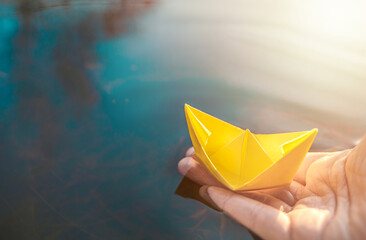 Yellow lonely floating paper boat in hand. Colorful sailing ship in big blue spring puddle, river...
